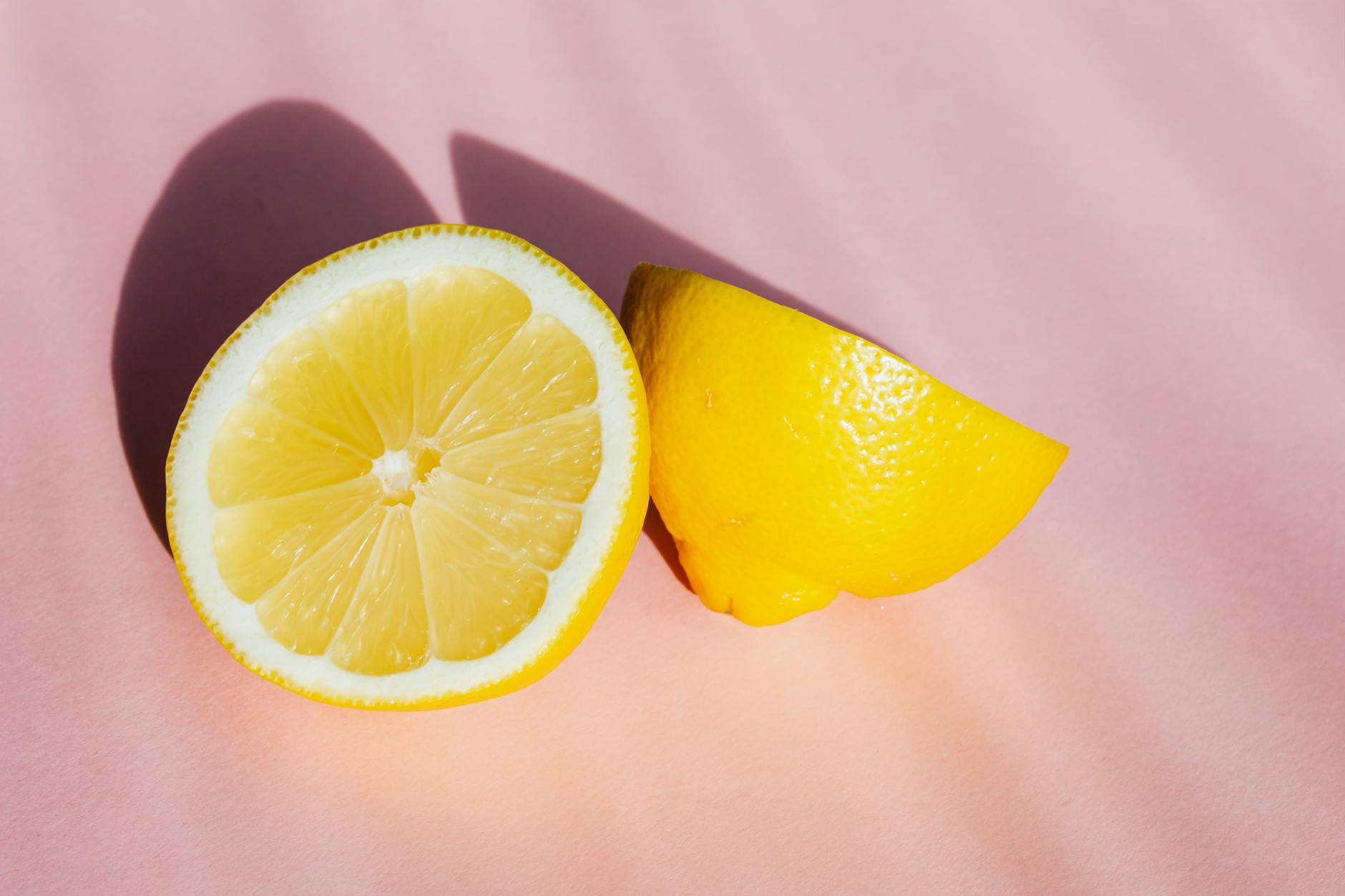 A hand holding a fresh lemon on a soft pink background, symbolizing freshness and pleasure