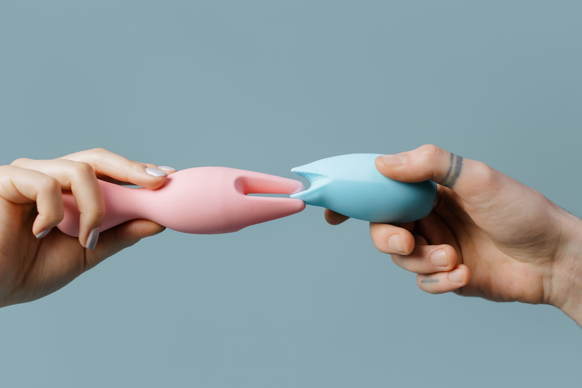 Hands holding pastel-colored silicone pleasure toys together