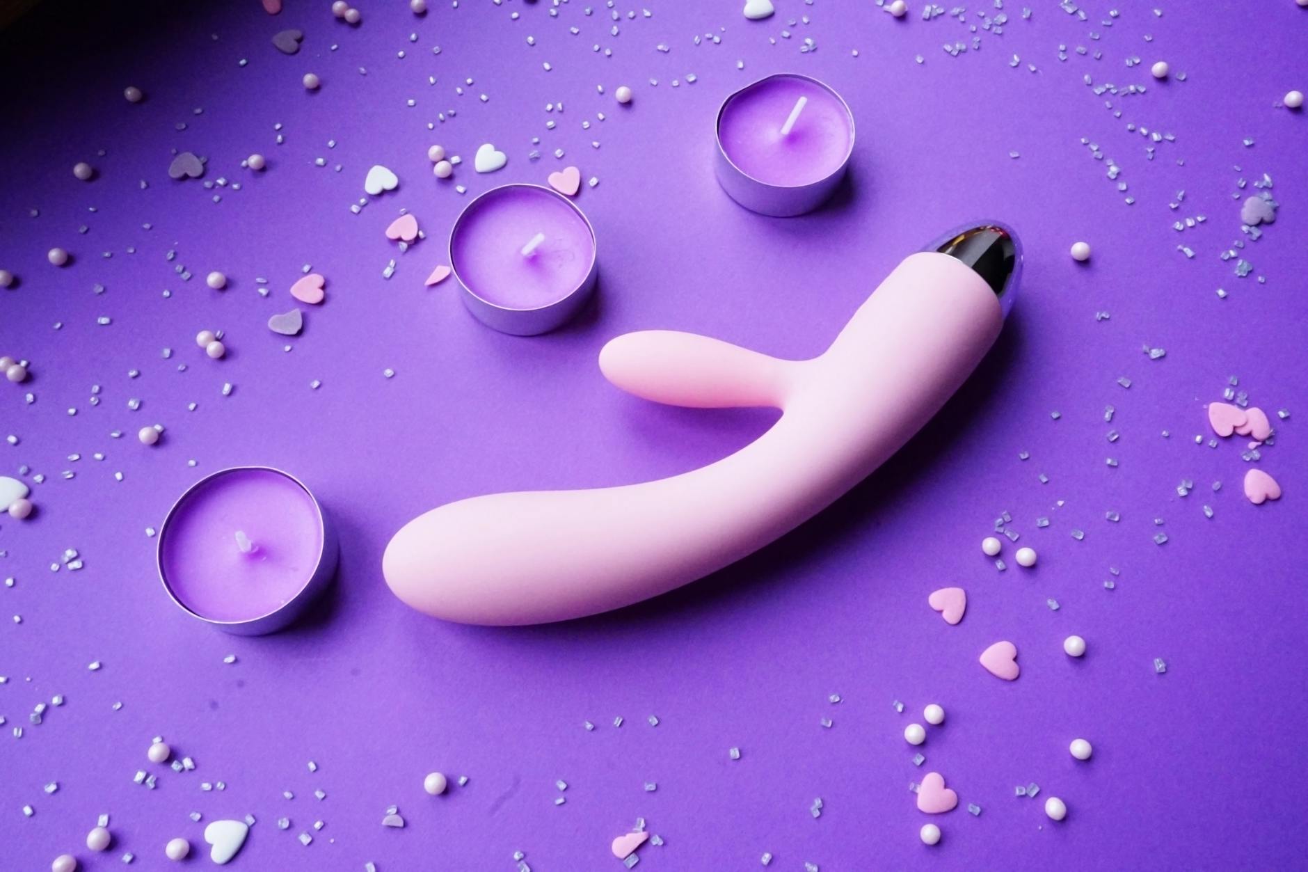 Pink lemon vibrator on purple background with heart confetti and candles for intimate recovery